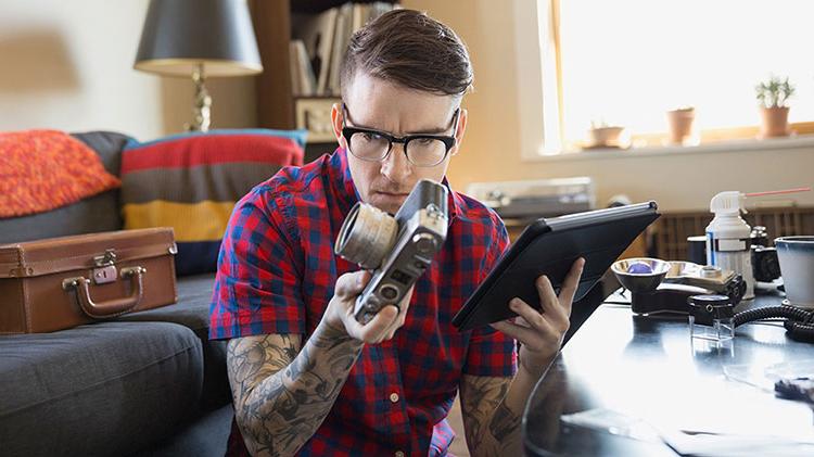 A man with glasses and a checkered flannel shirt inspects his camera.