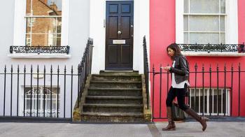 A woman approaches the stairs of a pink apartment building.